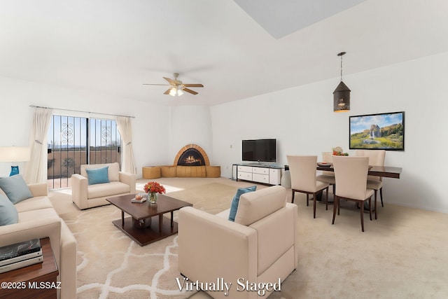 living room featuring carpet, a warm lit fireplace, and ceiling fan