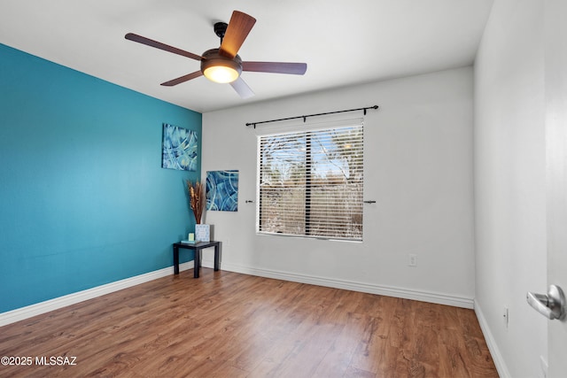 empty room with baseboards, wood finished floors, and a ceiling fan