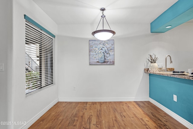 unfurnished dining area featuring wood finished floors, baseboards, and a sink