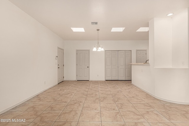 empty room with visible vents, a chandelier, a skylight, baseboards, and light tile patterned floors