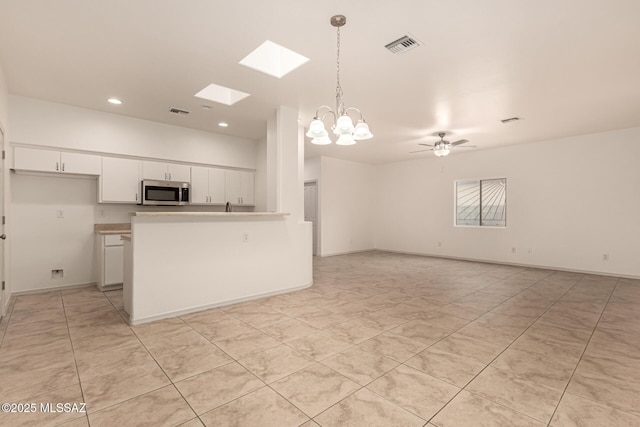 kitchen with pendant lighting, white cabinetry, a skylight, open floor plan, and stainless steel microwave