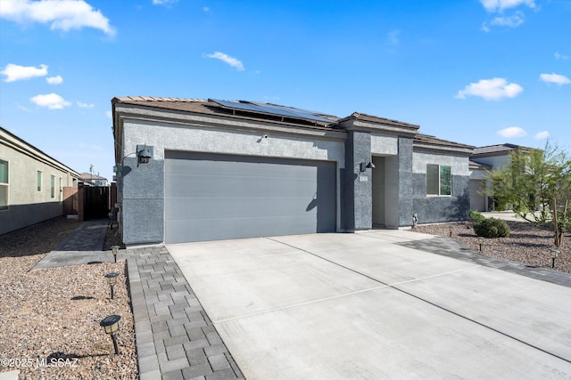 prairie-style home with stucco siding, driveway, fence, a garage, and solar panels