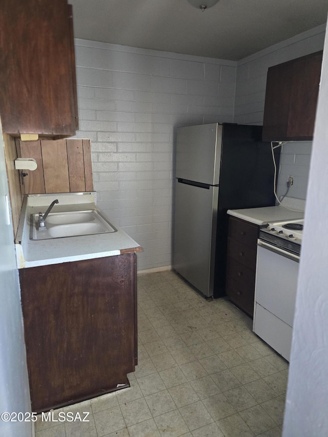 kitchen with electric range, a sink, light countertops, freestanding refrigerator, and light floors