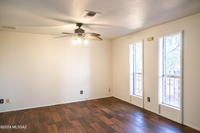 spare room with a textured ceiling, dark wood-type flooring, visible vents, and baseboards