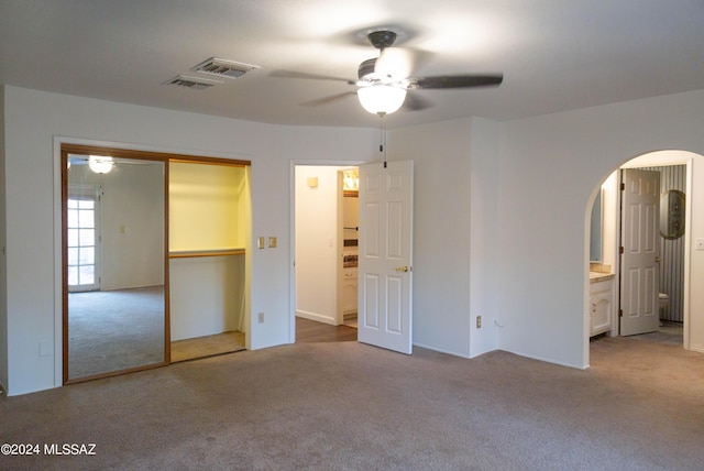 unfurnished bedroom featuring arched walkways, ensuite bath, ceiling fan, carpet flooring, and a closet