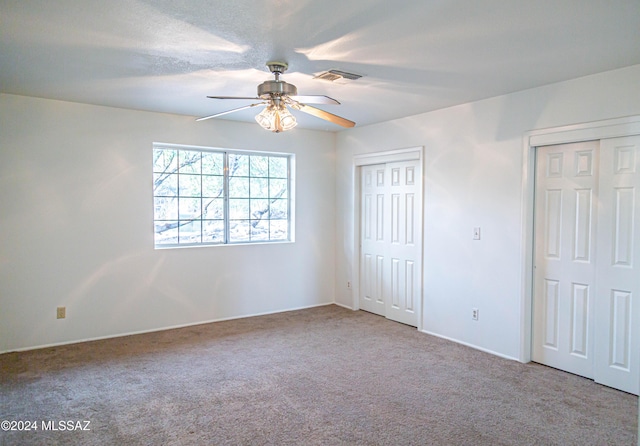 unfurnished bedroom featuring carpet floors, a ceiling fan, visible vents, and two closets