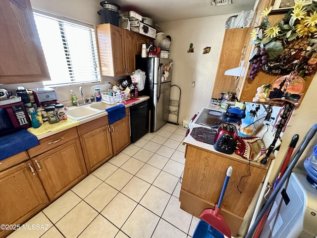 kitchen with light tile patterned floors, black dishwasher, freestanding refrigerator, light countertops, and a sink