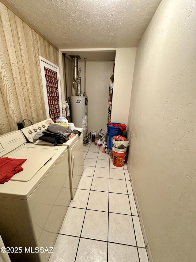 laundry area featuring light tile patterned floors, a textured ceiling, wood walls, washer and dryer, and water heater