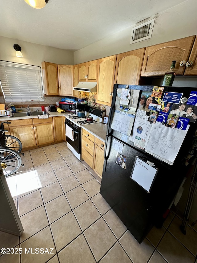 kitchen with visible vents, gas range, freestanding refrigerator, under cabinet range hood, and light tile patterned flooring