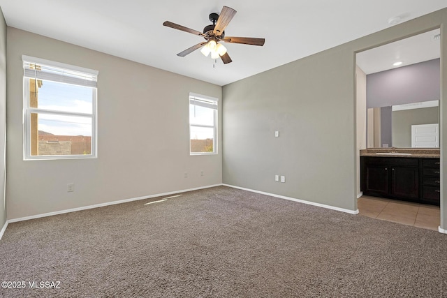 unfurnished bedroom with connected bathroom, light colored carpet, a sink, a ceiling fan, and baseboards