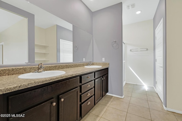 bathroom with double vanity, a walk in closet, a sink, and tile patterned floors