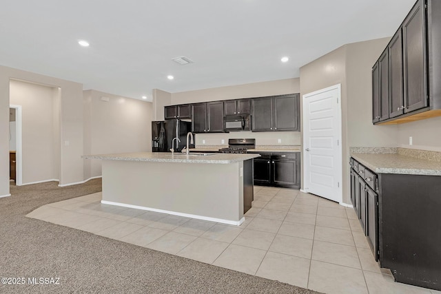 kitchen with light tile patterned floors, a center island with sink, light countertops, black appliances, and a sink