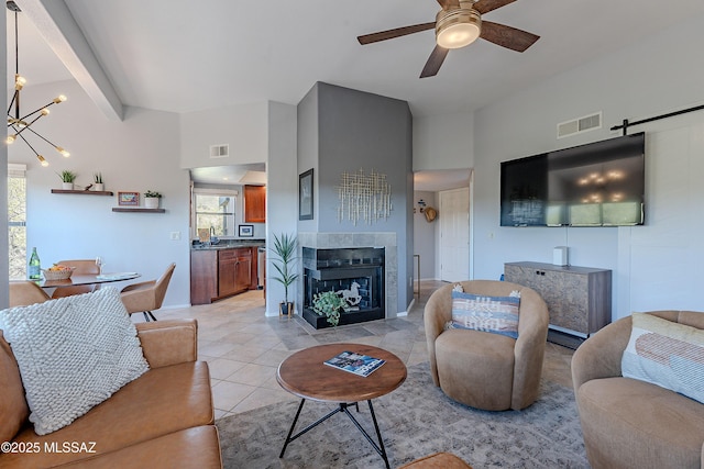 living room with a tiled fireplace, light tile patterned flooring, ceiling fan with notable chandelier, and visible vents