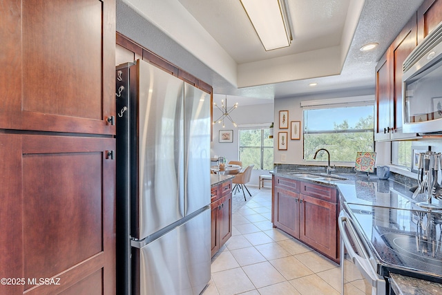 kitchen featuring dark stone countertops, light tile patterned flooring, a sink, appliances with stainless steel finishes, and a raised ceiling