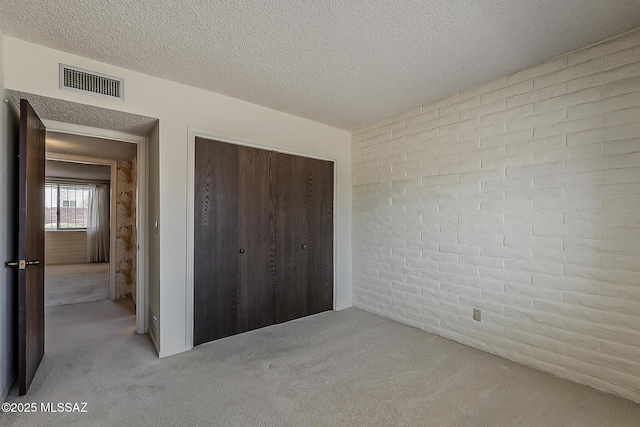 unfurnished bedroom with a textured ceiling, a closet, carpet flooring, and visible vents