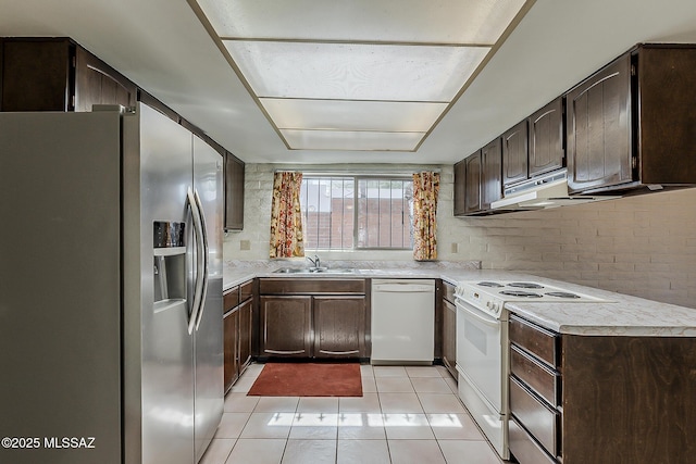 kitchen with a sink, light tile patterned floors, dark brown cabinets, and white appliances