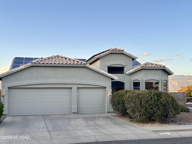 mediterranean / spanish house with a tile roof, solar panels, stucco siding, a garage, and driveway