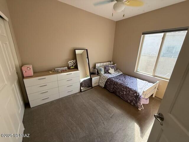 bedroom with ceiling fan, dark colored carpet, and a closet