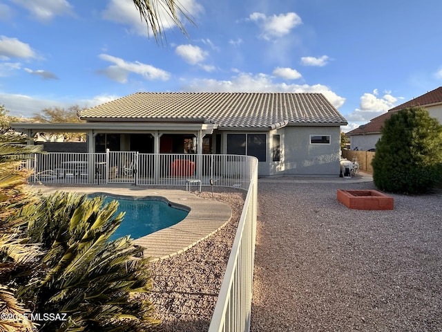 rear view of property featuring a patio, an outdoor fire pit, a tile roof, fence, and a fenced in pool