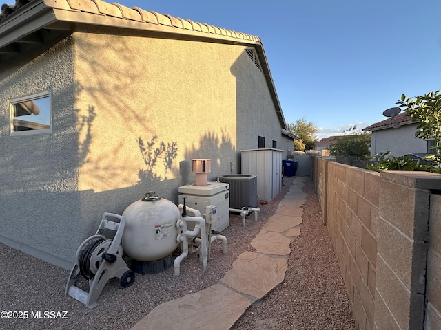 view of side of home with a tile roof, stucco siding, fence, and central AC unit