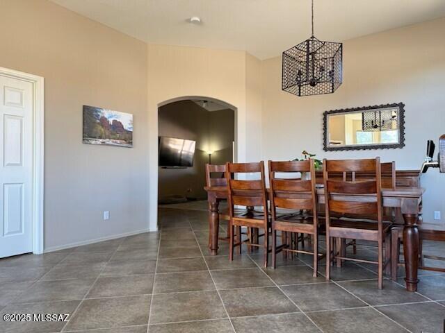 dining space with arched walkways, dark tile patterned flooring, baseboards, and a notable chandelier