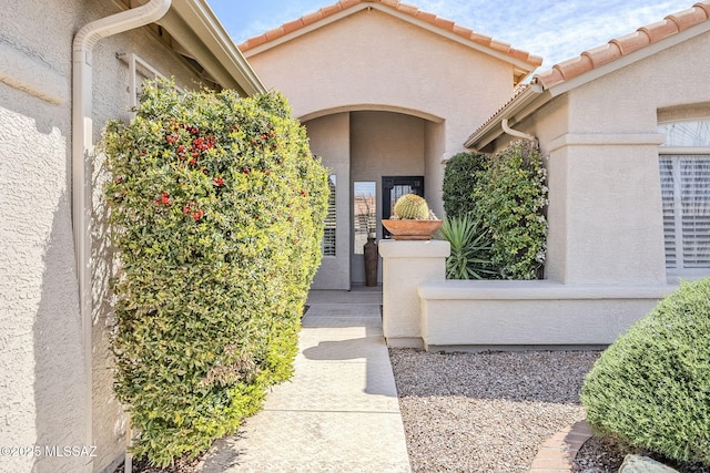 view of exterior entry with stucco siding and a tiled roof