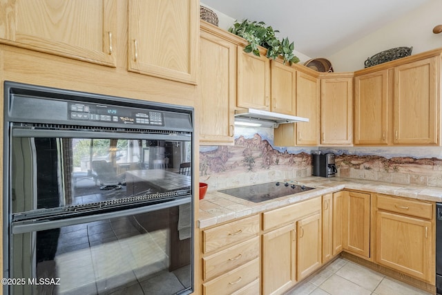 kitchen featuring under cabinet range hood, light brown cabinets, black appliances, and tile counters