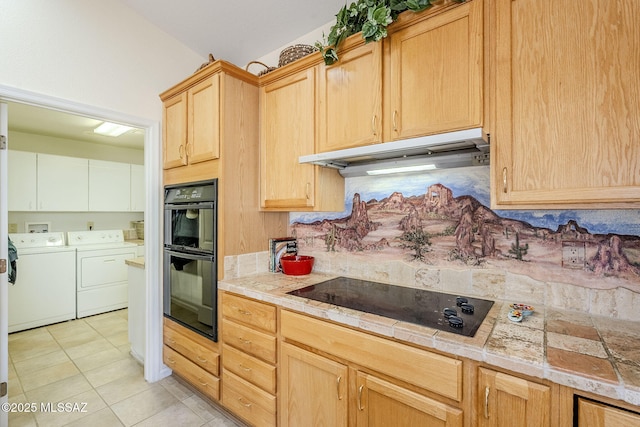 kitchen with light brown cabinets, under cabinet range hood, washer and clothes dryer, light tile patterned flooring, and black appliances