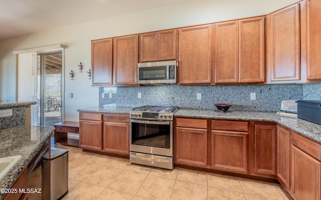 kitchen featuring backsplash, stone counters, brown cabinets, light tile patterned flooring, and stainless steel appliances