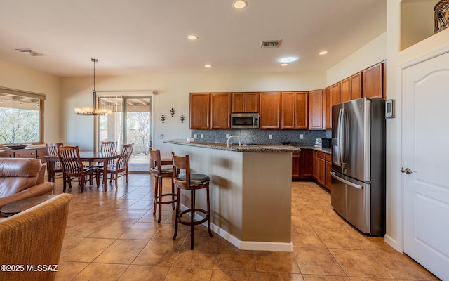 kitchen featuring a breakfast bar area, brown cabinets, backsplash, and stainless steel appliances