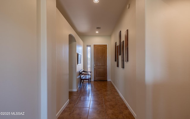 hallway featuring tile patterned flooring, recessed lighting, arched walkways, and baseboards