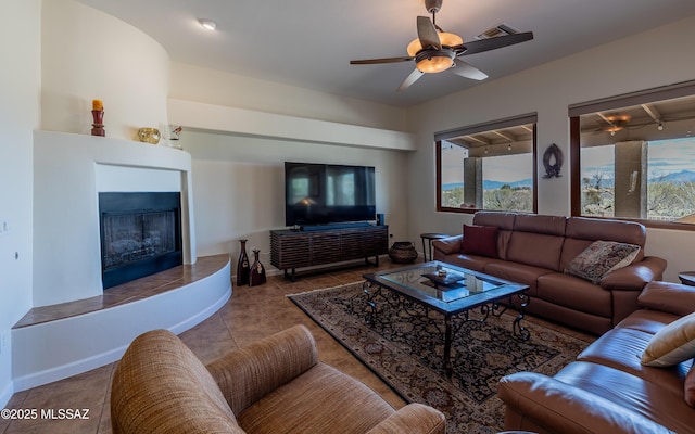 tiled living area featuring visible vents, a fireplace with raised hearth, baseboards, and a ceiling fan