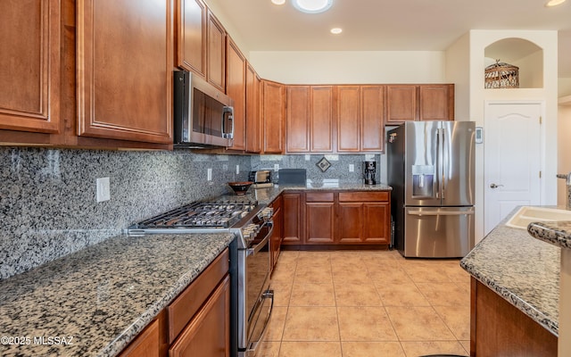 kitchen with brown cabinets, a sink, tasteful backsplash, appliances with stainless steel finishes, and light tile patterned floors