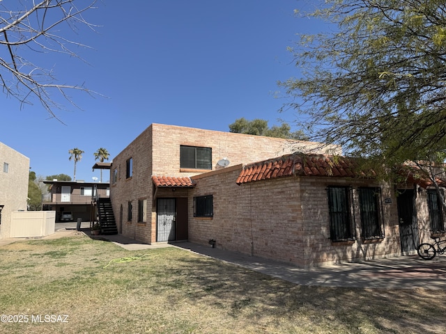 back of house featuring a tile roof, fence, a lawn, and stairs