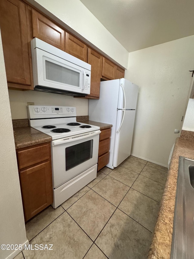 kitchen featuring dark countertops, white appliances, light tile patterned flooring, and brown cabinets