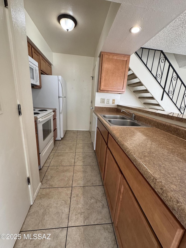 kitchen with white appliances, light tile patterned floors, brown cabinets, and a sink