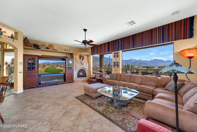 living area featuring visible vents, plenty of natural light, a large fireplace, and a ceiling fan