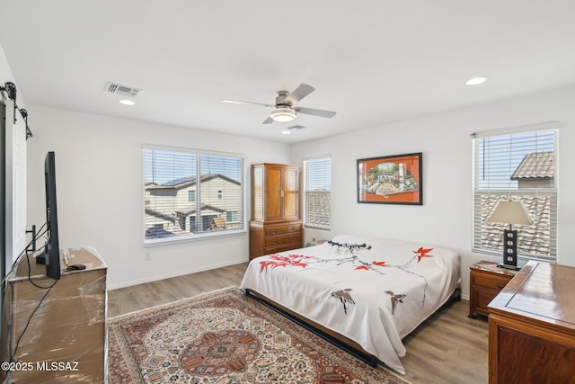 bedroom with visible vents, multiple windows, light wood-type flooring, and a barn door