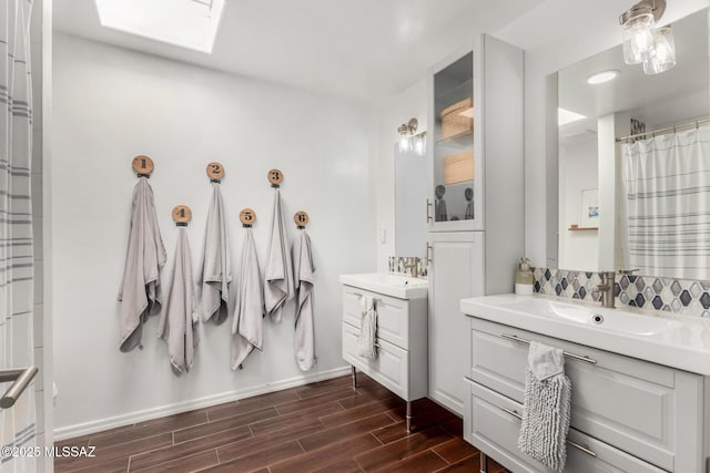 bathroom with a skylight, two vanities, a sink, baseboards, and wood tiled floor