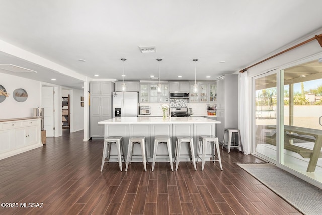 kitchen featuring visible vents, dark wood finished floors, glass insert cabinets, a breakfast bar area, and stainless steel appliances