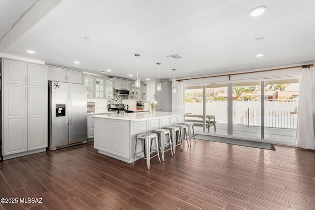 kitchen with a breakfast bar, wood finish floors, light countertops, appliances with stainless steel finishes, and glass insert cabinets