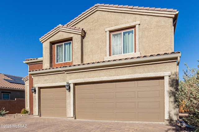 view of front of house featuring a garage, decorative driveway, a tiled roof, and stucco siding