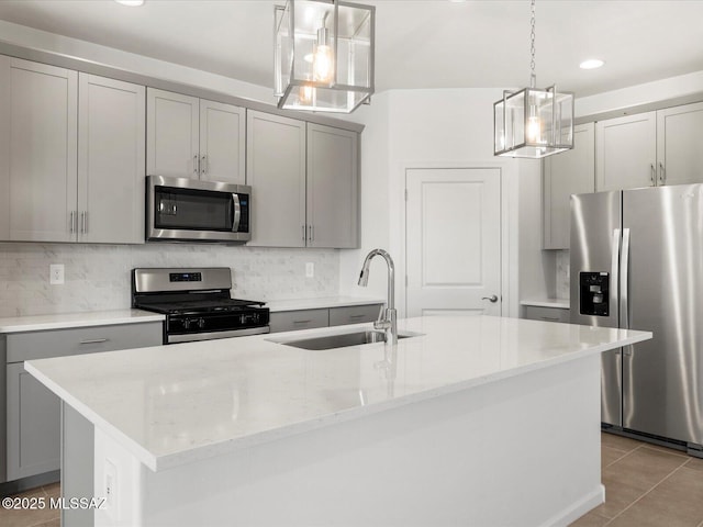 kitchen featuring appliances with stainless steel finishes, a sink, gray cabinets, a kitchen island with sink, and backsplash