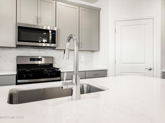 kitchen featuring appliances with stainless steel finishes, gray cabinets, decorative backsplash, and a sink