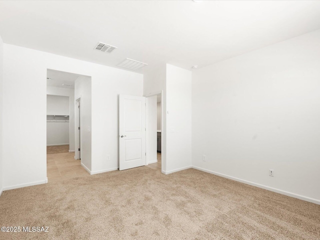 unfurnished bedroom with light colored carpet, a walk in closet, baseboards, and a closet