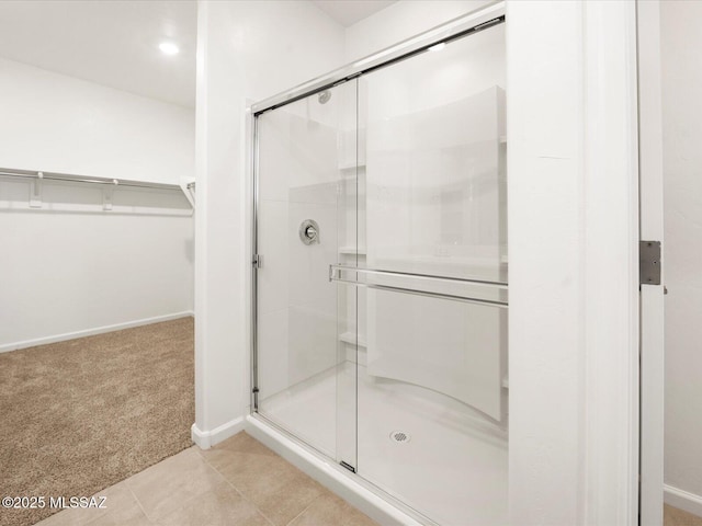 bathroom with a stall shower, a walk in closet, baseboards, and tile patterned floors