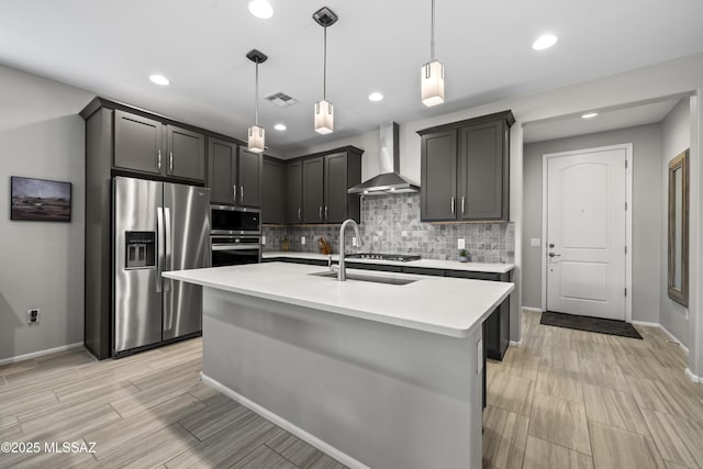 kitchen featuring tasteful backsplash, light countertops, appliances with stainless steel finishes, a sink, and wall chimney exhaust hood