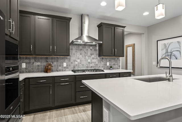 kitchen with wall chimney exhaust hood, appliances with stainless steel finishes, light countertops, and a sink