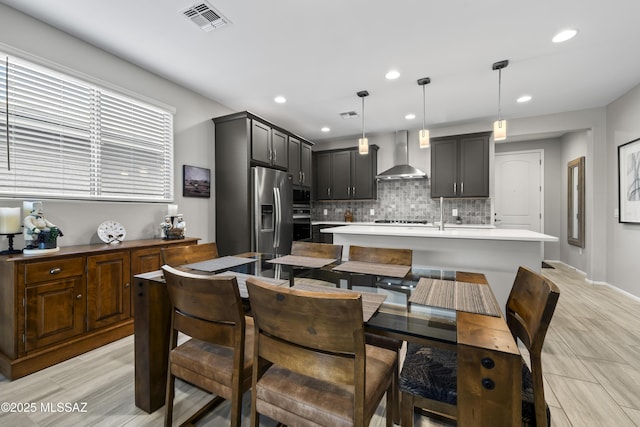 kitchen featuring tasteful backsplash, stainless steel fridge, visible vents, an island with sink, and wall chimney exhaust hood