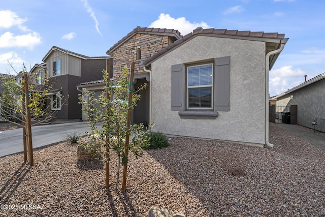 view of front of property featuring driveway, stone siding, a tiled roof, and stucco siding